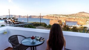 A balcony with a table and chairs overlooking a coastal landscape with cliffs and a body of water. - Sigal Villa (Santorini)