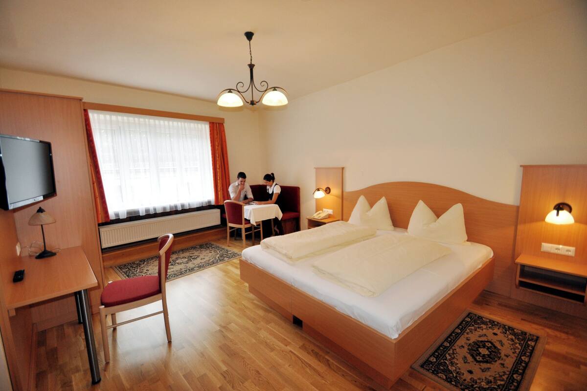 A hotel room with a bed, a desk, a chair, a television, and a window with curtains.