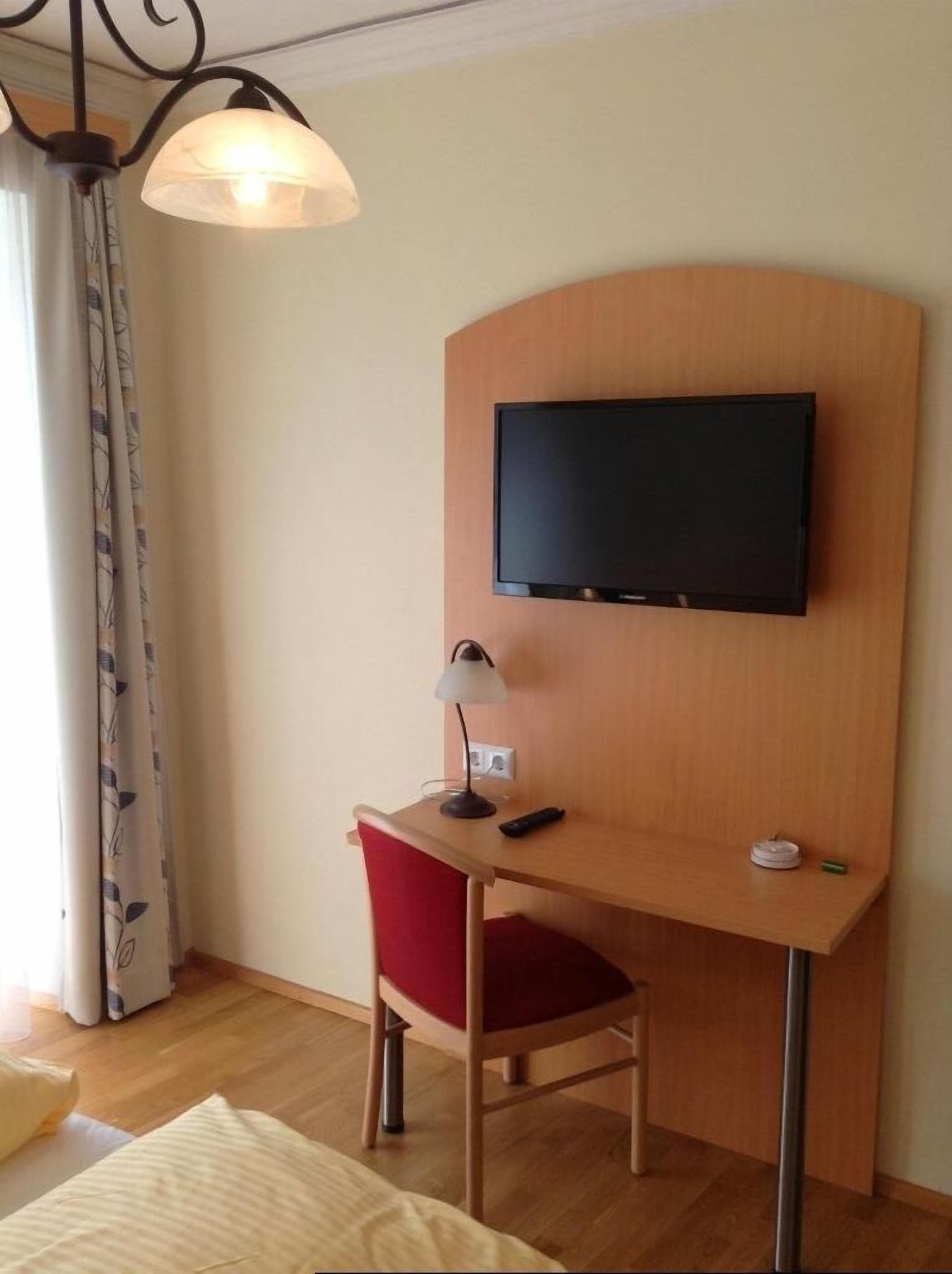 A compact room with a foldable bed, a small desk with a laptop, a chair, and a wall-mounted lamp.