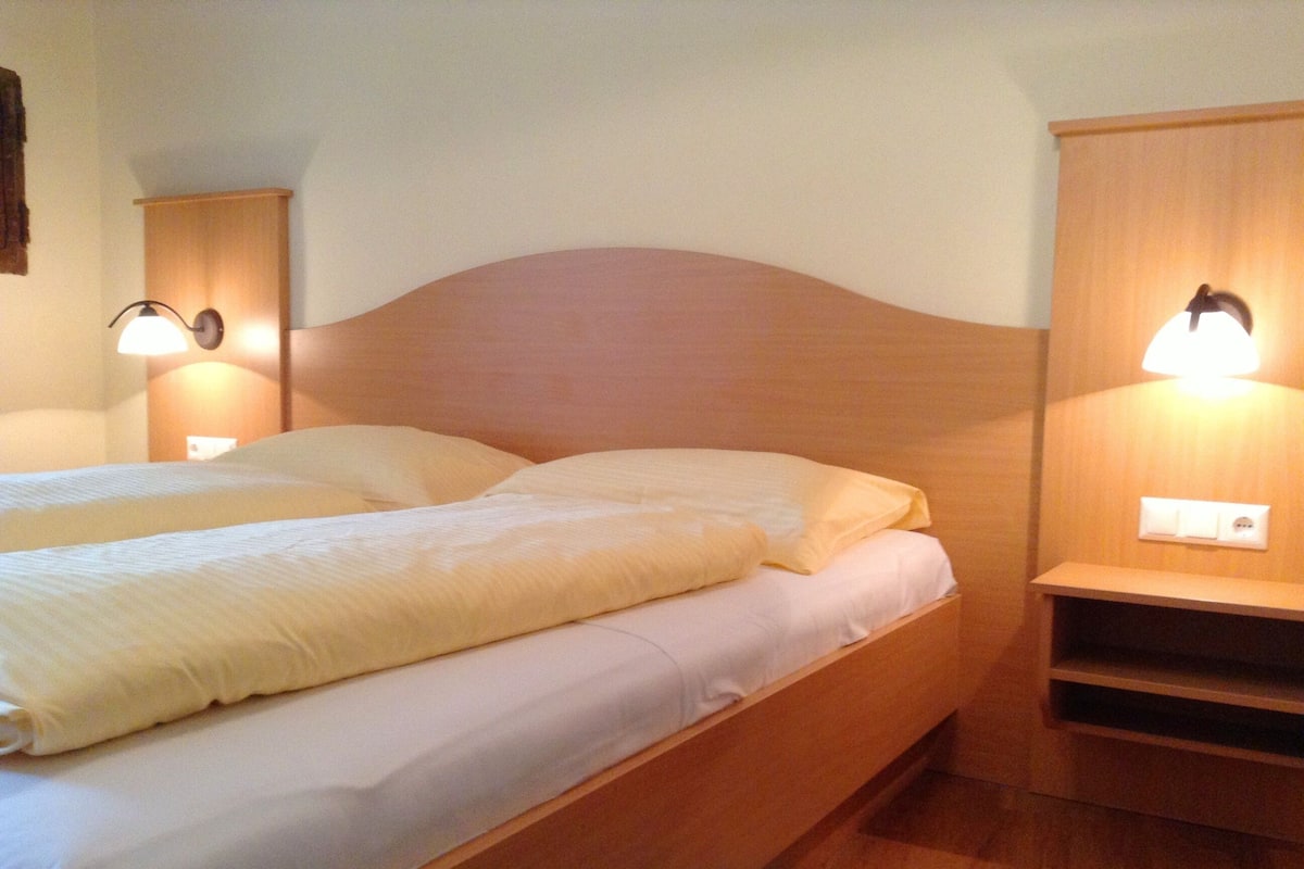 A double bed with white bedding, wooden headboard, bedside tables with lamps, and a wooden nightstand.