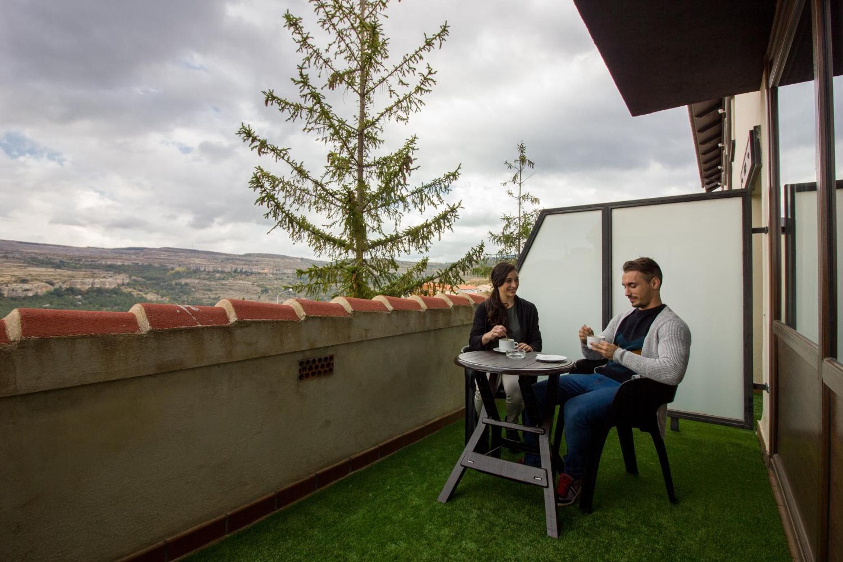 Dues persones assegudes a una taula en una terrassa al terrat amb vista al paisatge.