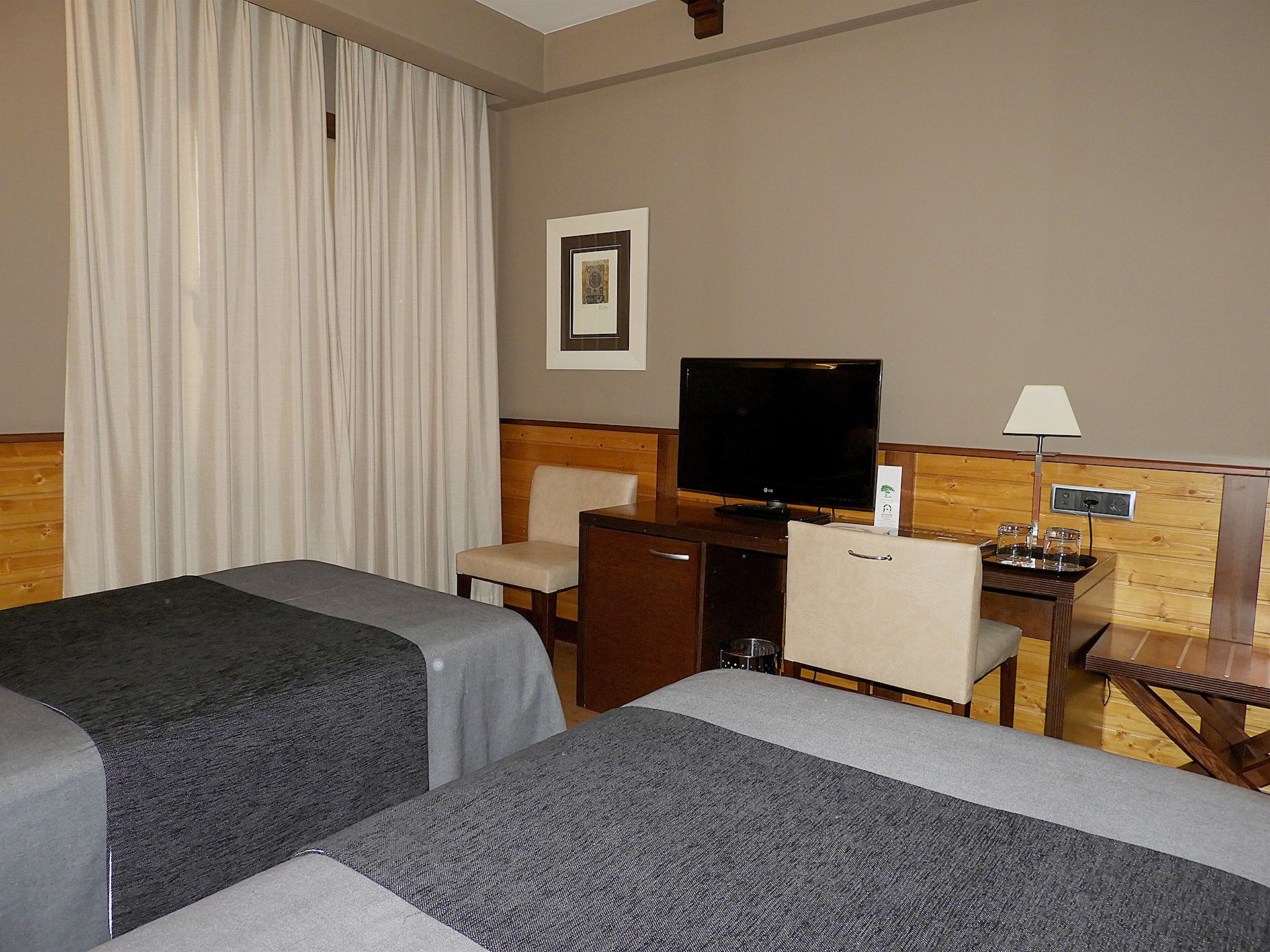 Una habitación de hotel con dos camas, un escritorio con televisor, una lámpara y un cuadro en la pared.