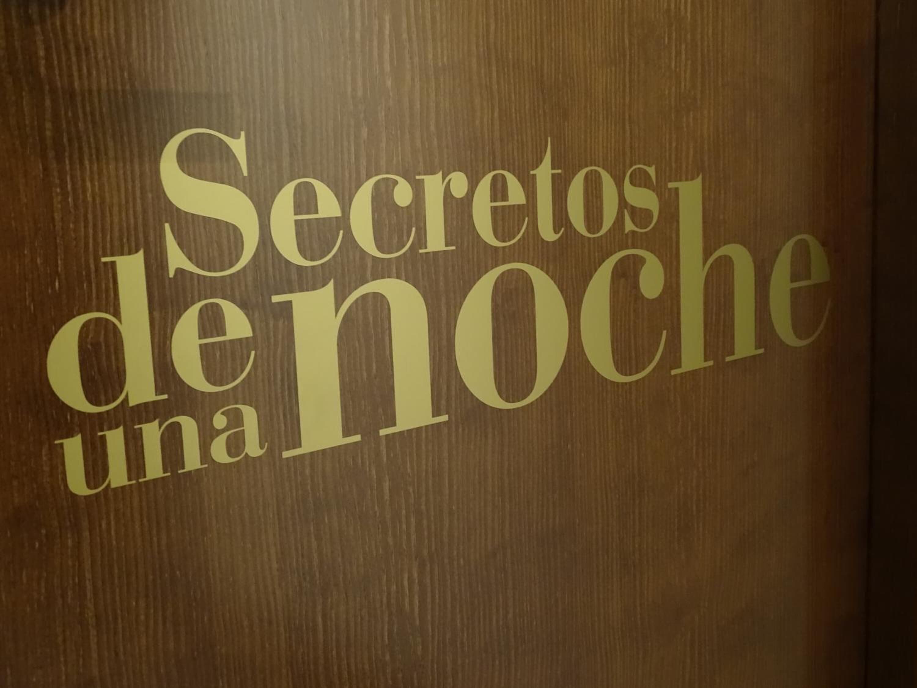 Una porta di legno con la scritta "Secretos de noche una" in caratteri dorati.