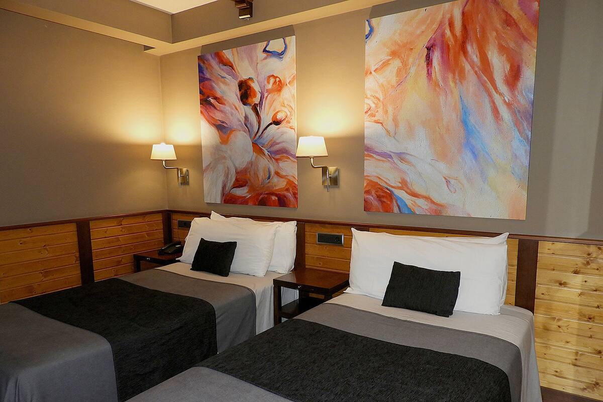 A hotel room with two beds, each with a pillow and a blanket. There are two wall-mounted lamps on either side of the beds.