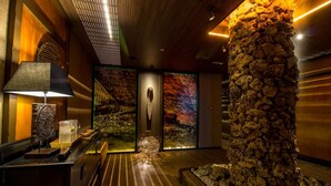 A modern lobby with a stone column, a reception desk, and a large wall with a nature-themed mural. - Hotel & Spa Balfagón (Cantavieja)