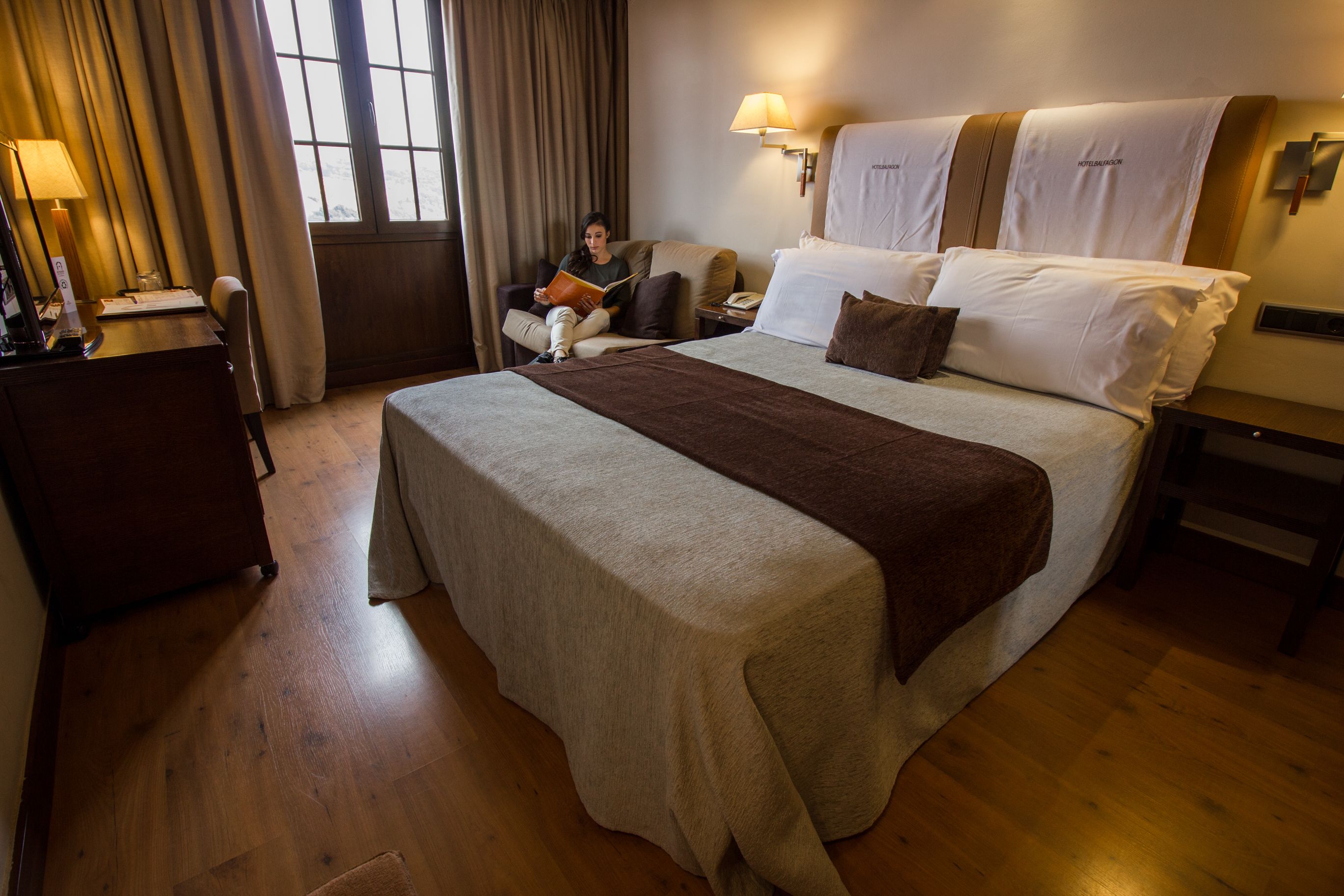 Een hotelkamer met een groot bed, een bureau, een stoel en een raam met gordijnen.