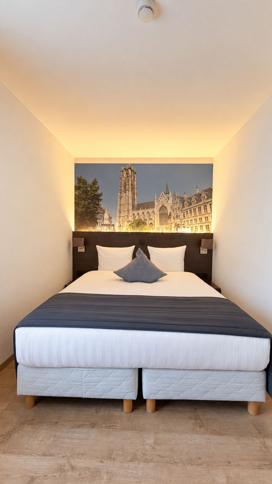 Ein Hotelzimmer mit einem großen Bett, einem Kopfteil mit Stadtbildmalerei und einem Holzboden.