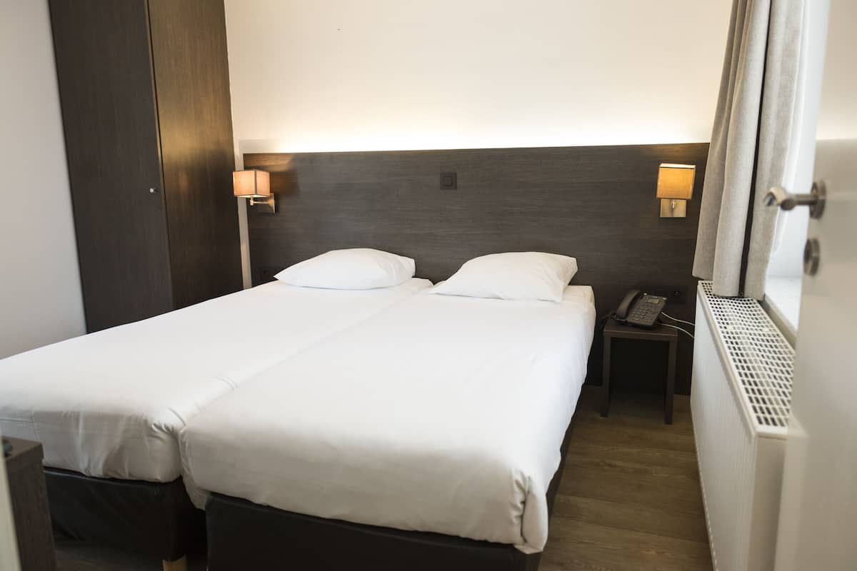 A hotel room with a double bed, bedside lamps, a telephone, and a radiator.
