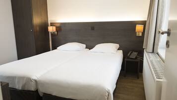 A hotel room with a double bed, bedside lamps, a telephone, and a radiator.