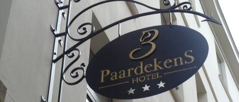 Un letrero del '3 Paardekens Hotel' con un marco de metal decorativo y estrellas debajo del nombre.