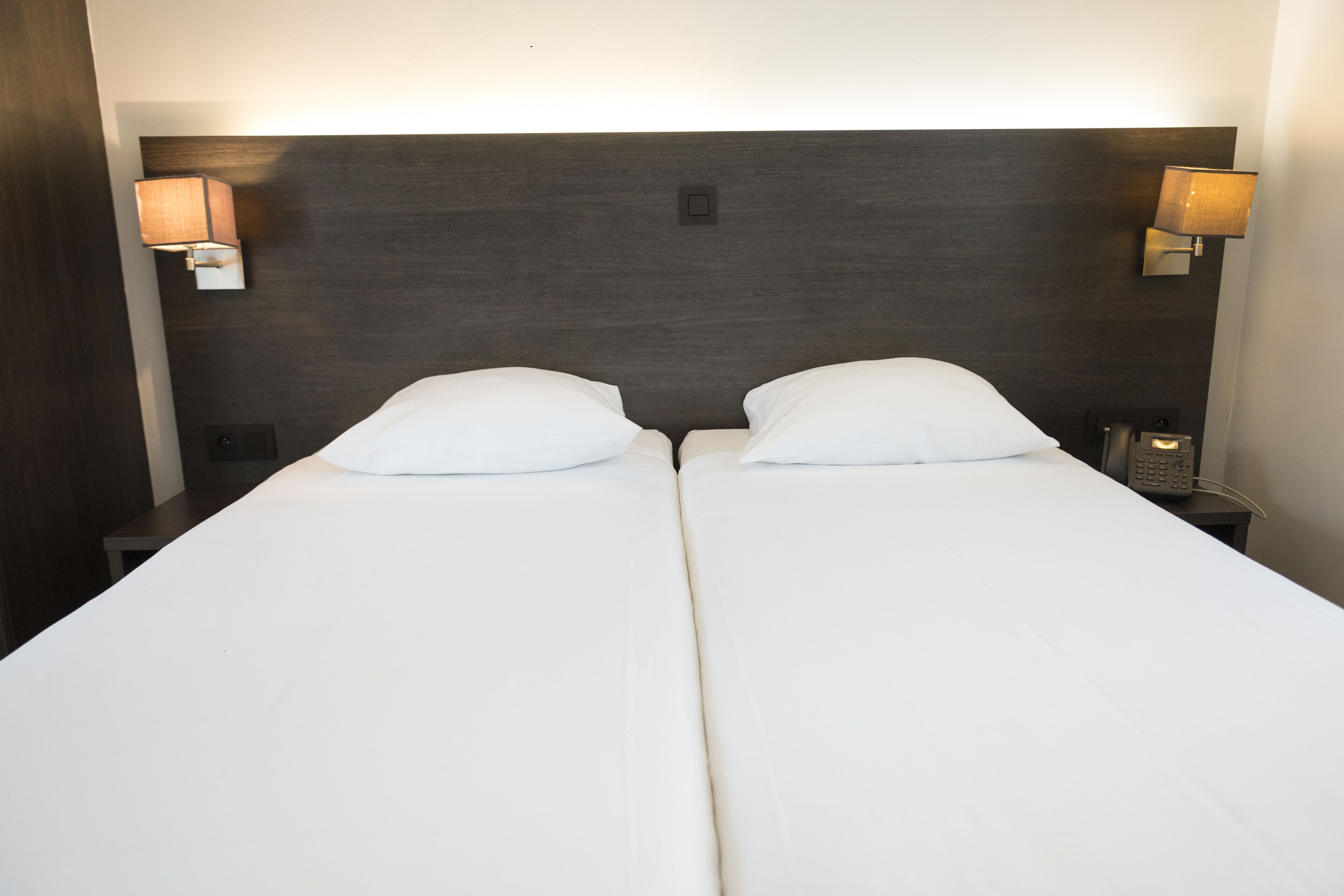 A double bed with white linens, two bedside tables with lamps, and a dark headboard.