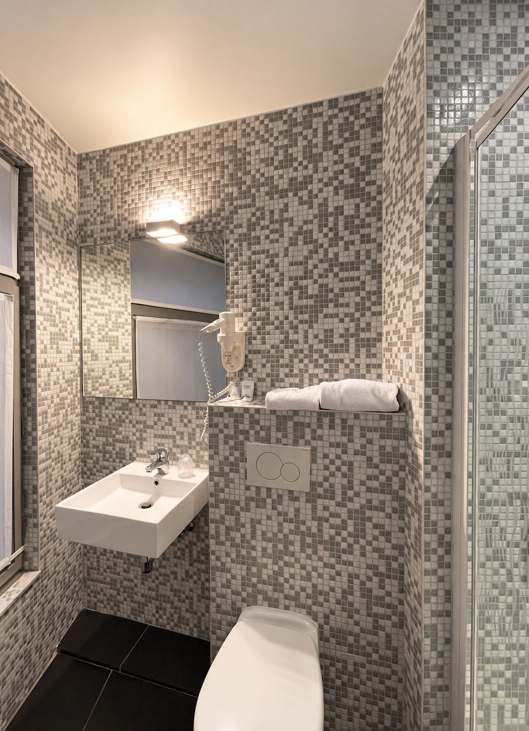 Een badkamer met een betegelde mozaïekwand, een wit wastafelmeubel, een spiegel, een handdoekhouder en een toilet.