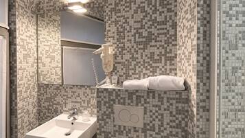 Een badkamer met een betegelde mozaïekwand, een wit wastafelmeubel, een spiegel, een handdoekhouder en een toilet.