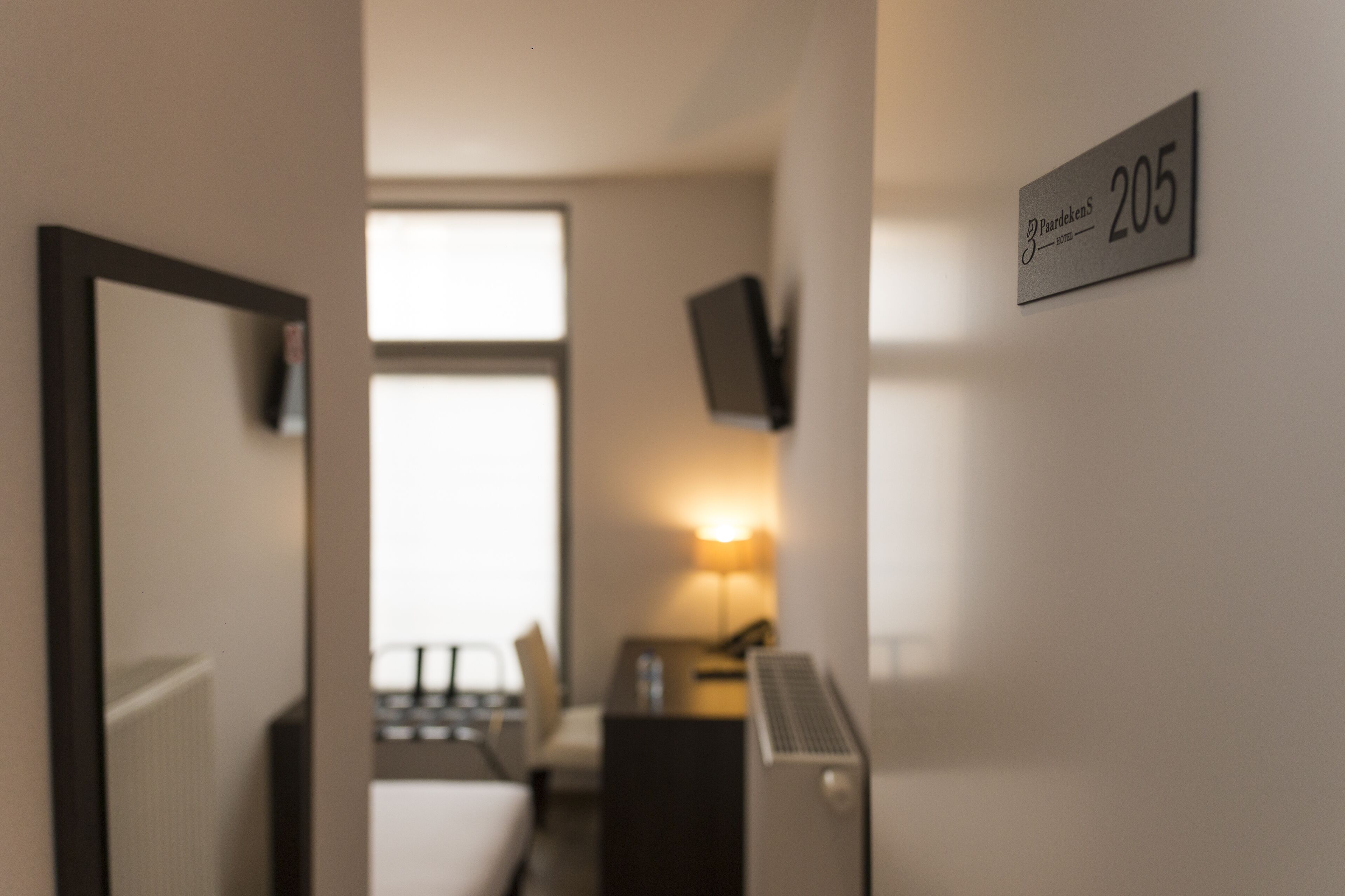 A hotel room with a bed, a desk, a lamp, and a TV on the wall.