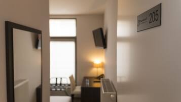 A hotel room with a bed, a desk, a lamp, and a TV on the wall.