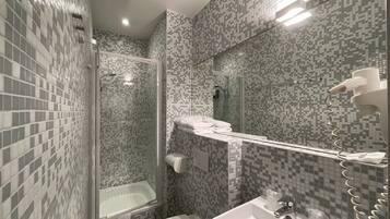 Une salle de bain équipée d’une douche, de toilettes et d’un lavabo, avec des murs recouverts de mosaïques et un miroir.