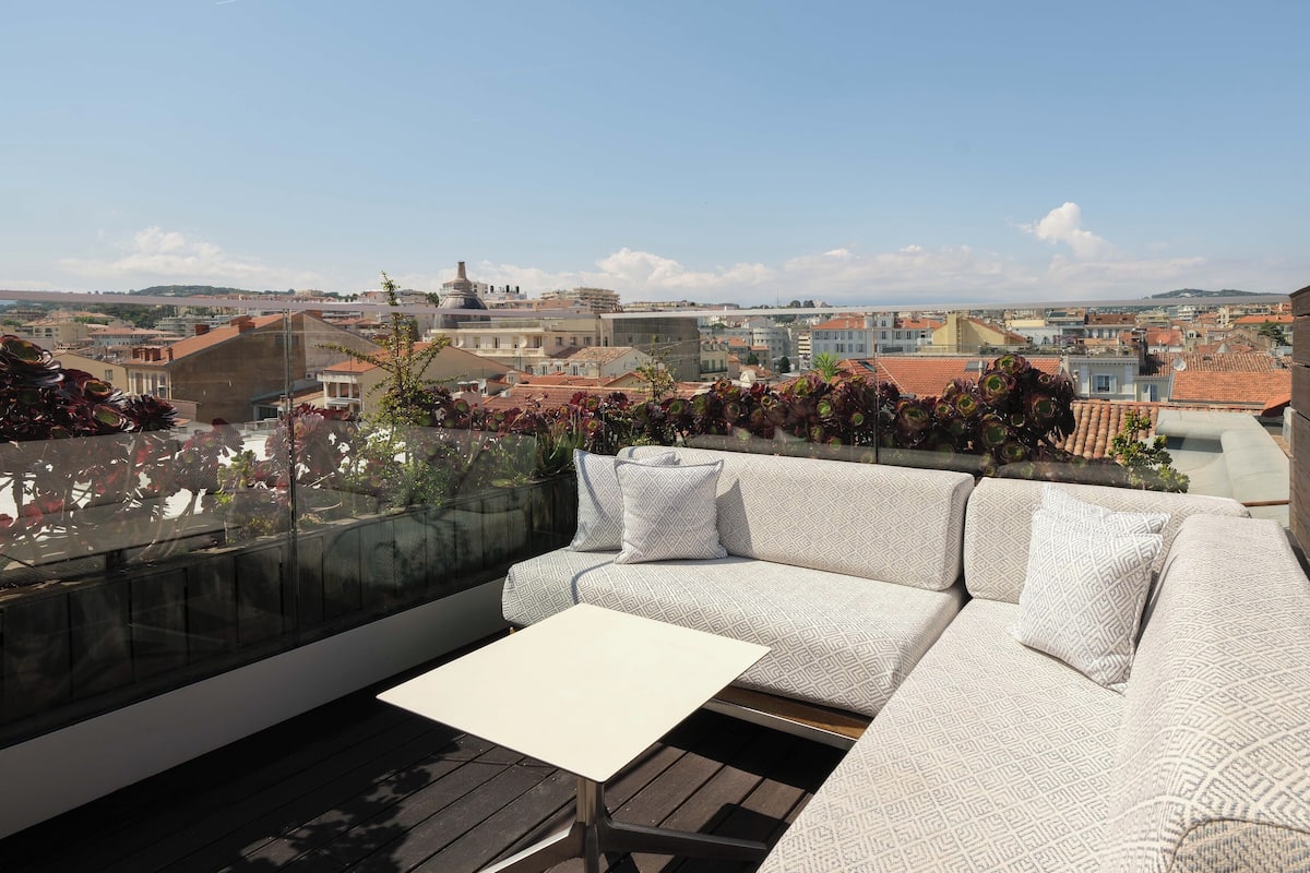 Terraza en la azotea con un sofá blanco, una mesita y barandilla de cristal con vistas a la ciudad.