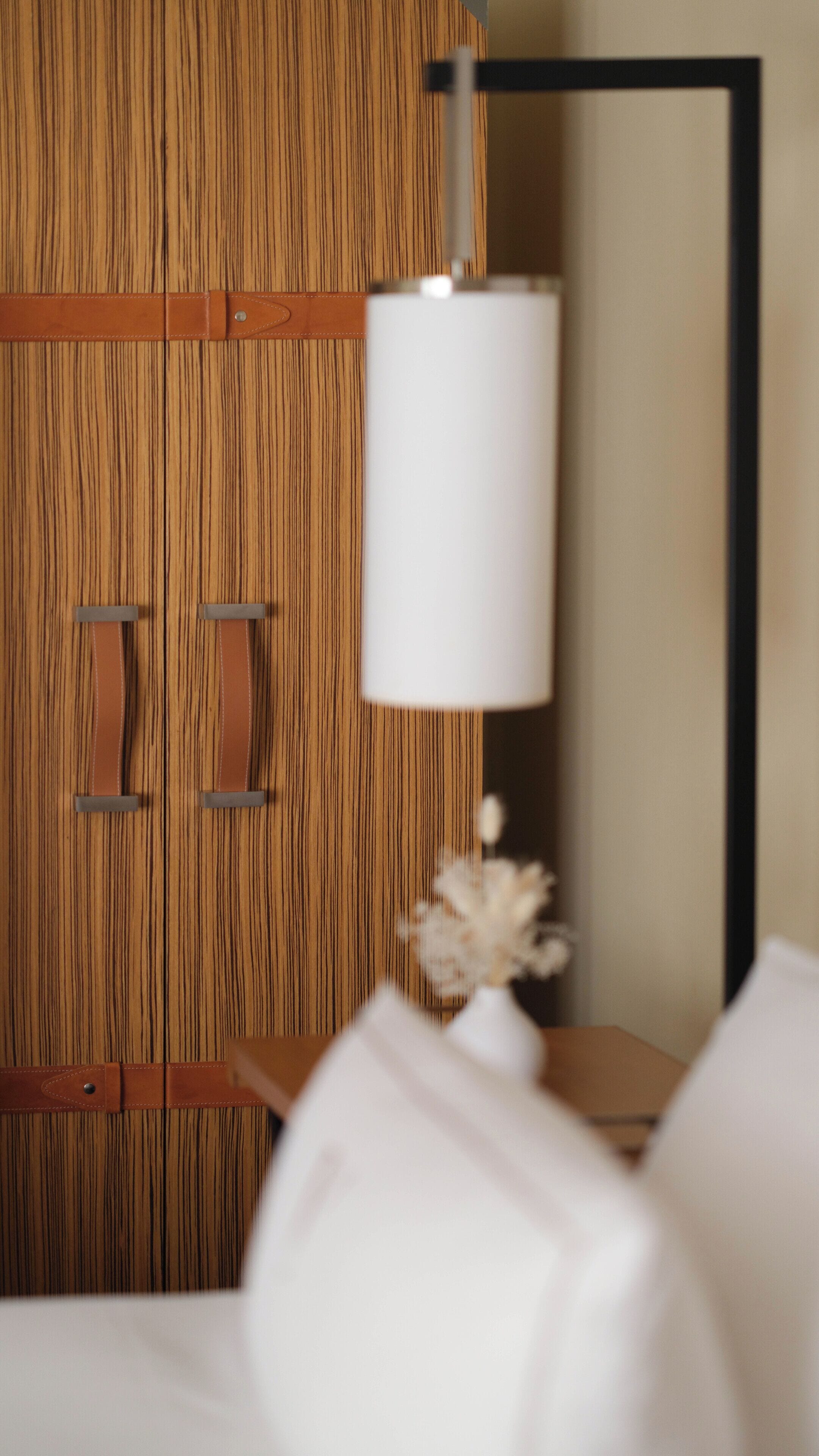 Ein Holzschrank mit zwei Griffen, eine weiße Lampe auf einem Nachttisch und ein Spiegel an der Wand.