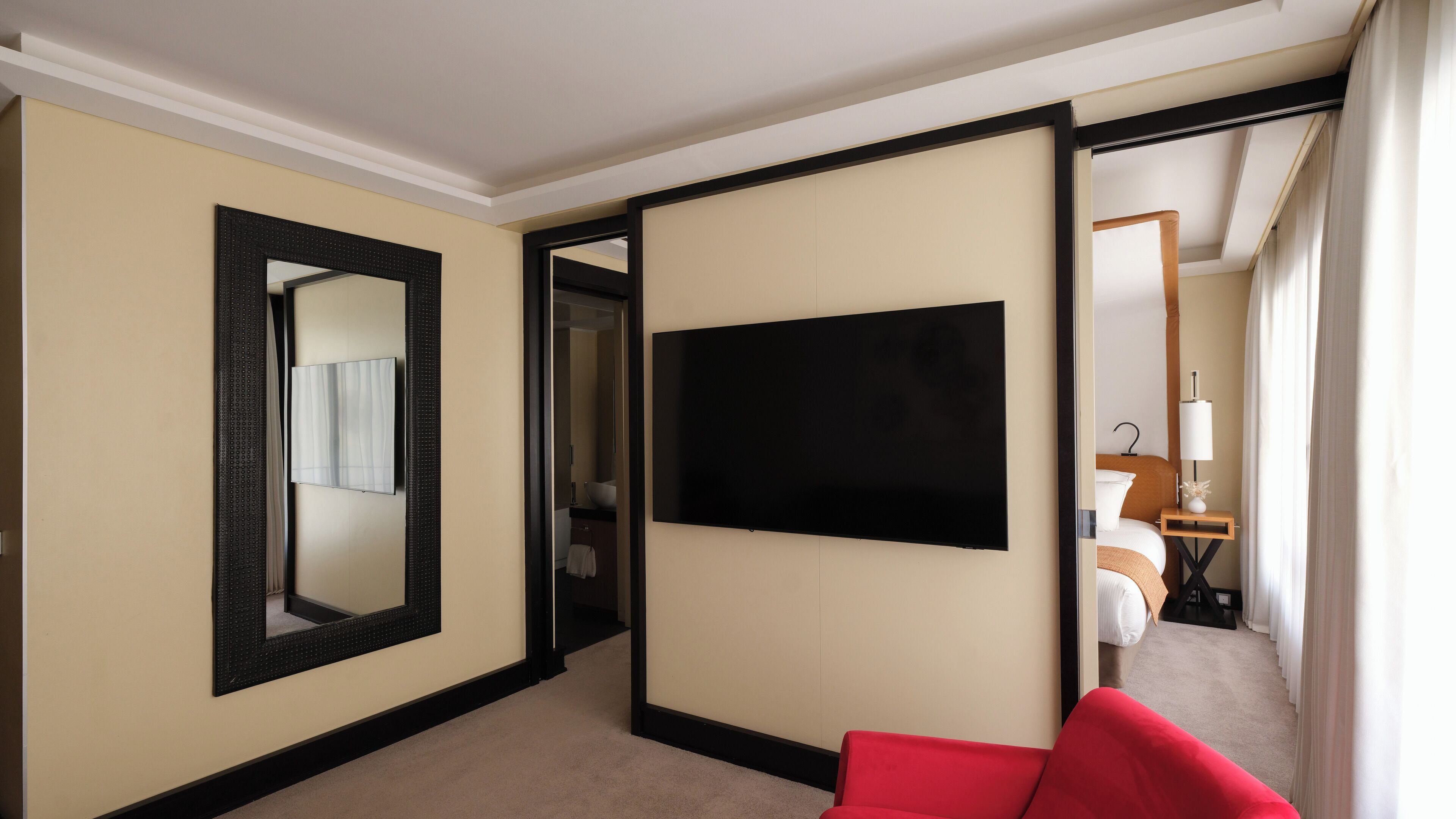 Ein Hotelzimmer mit einem großen Flachbildfernseher an der Wand, einem roten Sessel und einem großen Spiegel.