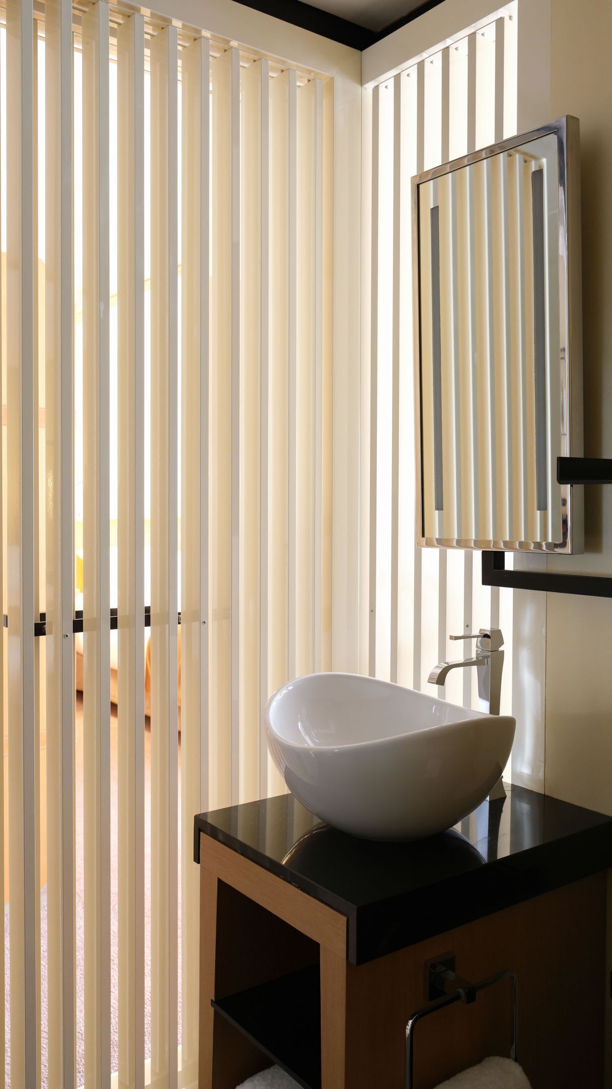 A bathroom with a white vessel sink, a mirror, and vertical blinds.