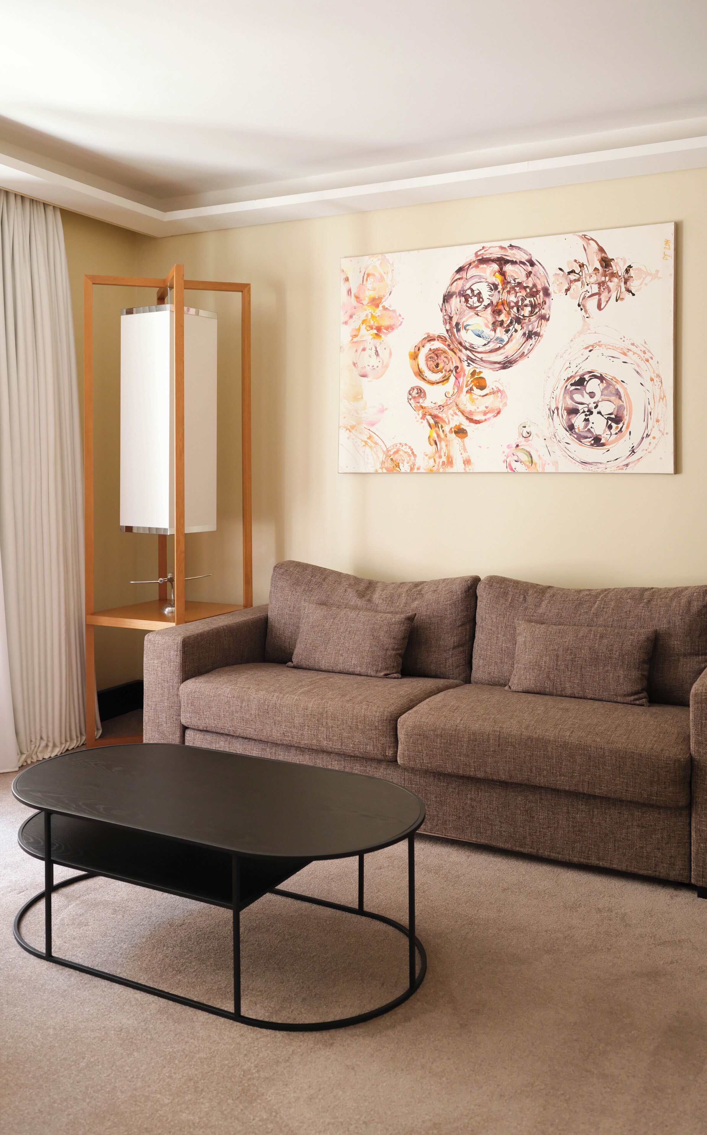 A modern living room with a brown sofa, a black coffee table, and a large abstract painting on the wall.