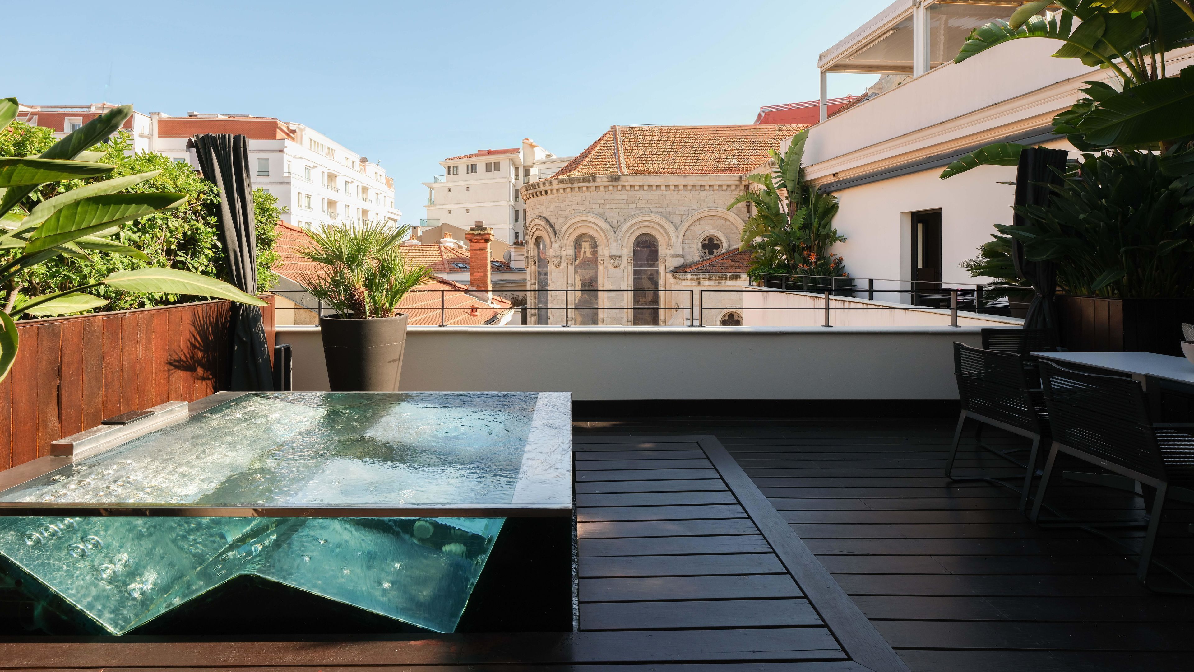Een terras op het dak met een hottub, houten terras en planten in potten.