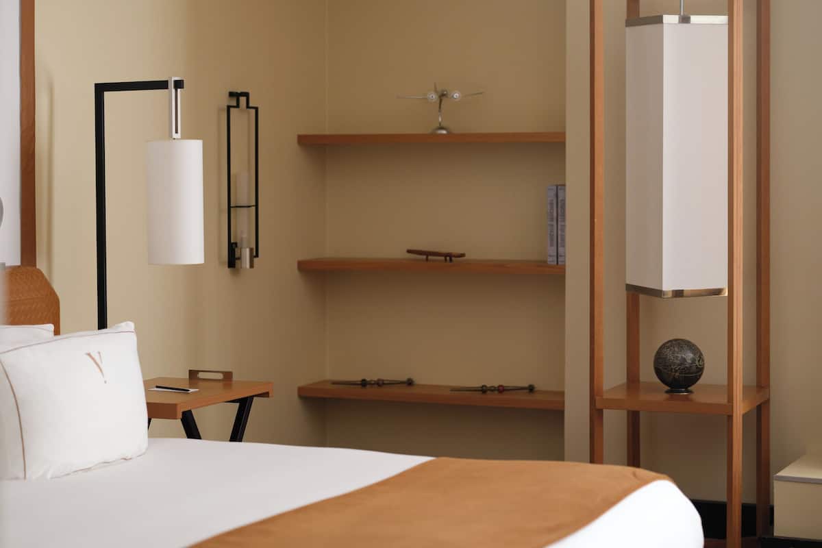Una habitación de hotel con una cama, un escritorio, estanterías y una lámpara.
