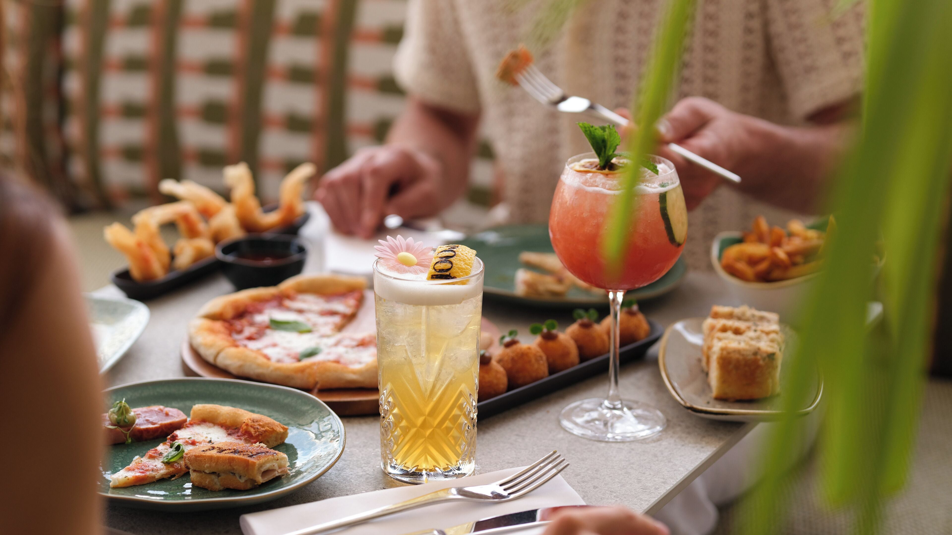 A dining table with various dishes, including pizza, bread, and a cocktail with a garnish.