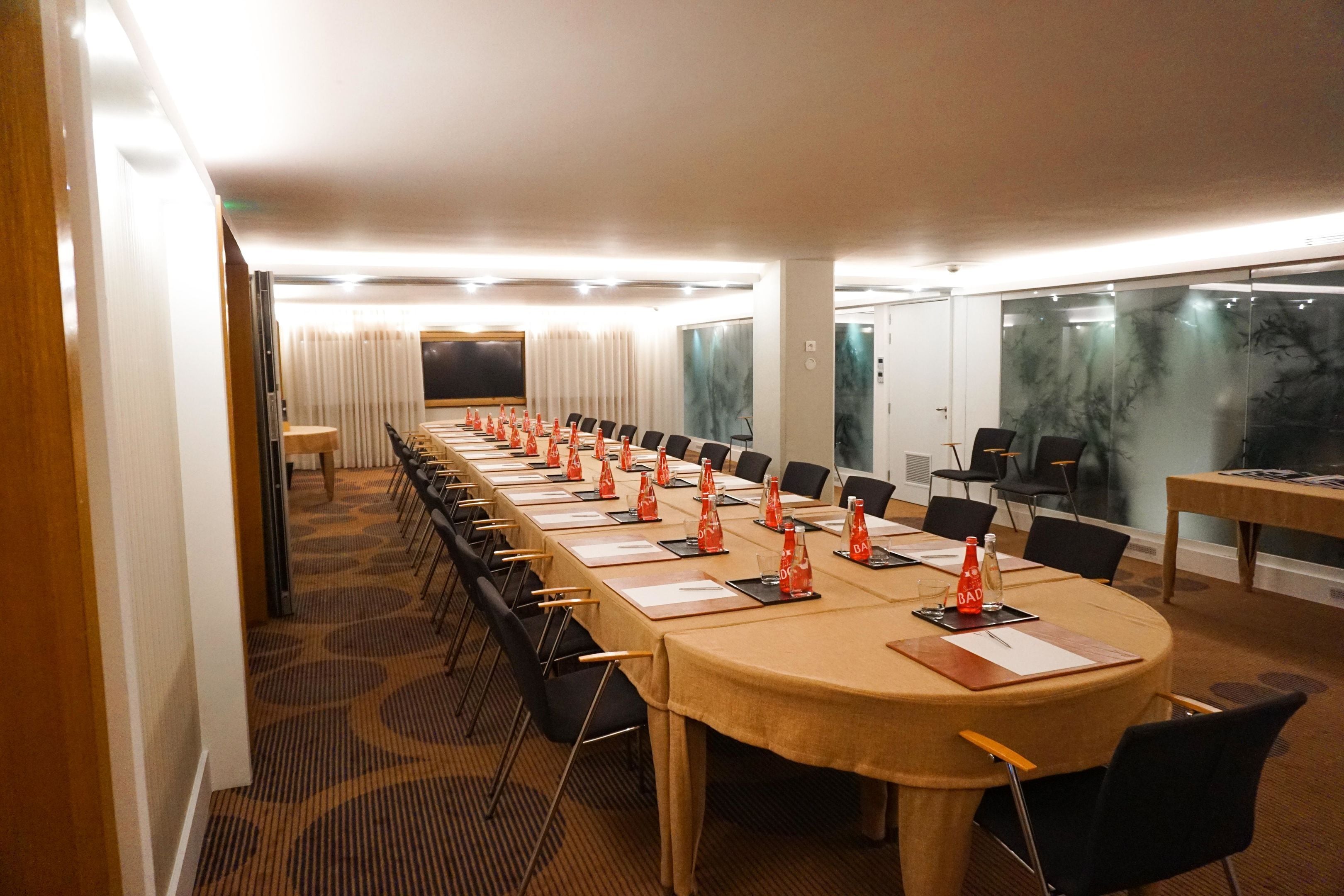 Una sala de conferencias con una larga mesa, sillas y una pantalla para proyector.
