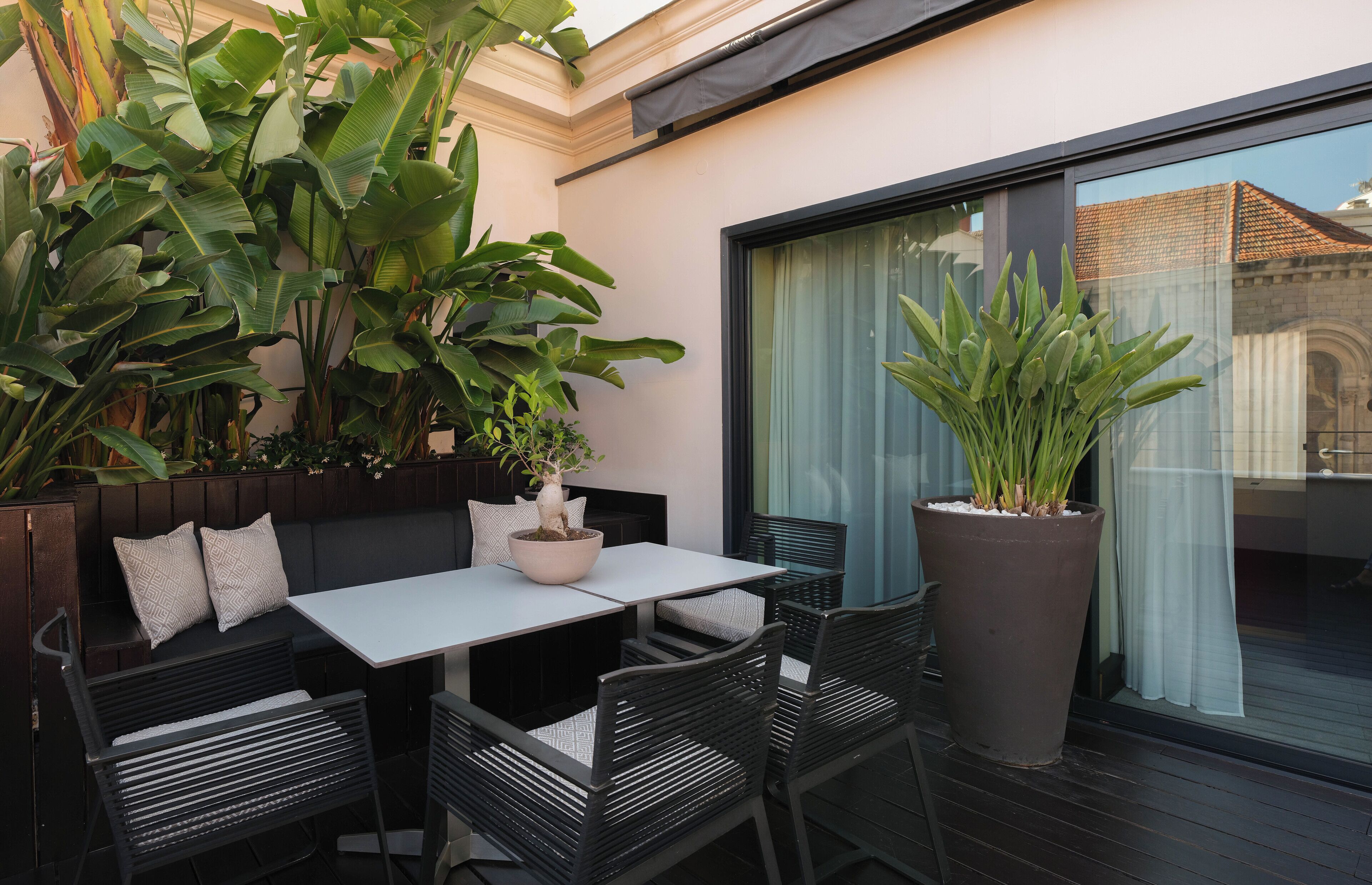 An outdoor patio with a table and chairs, surrounded by large potted plants.