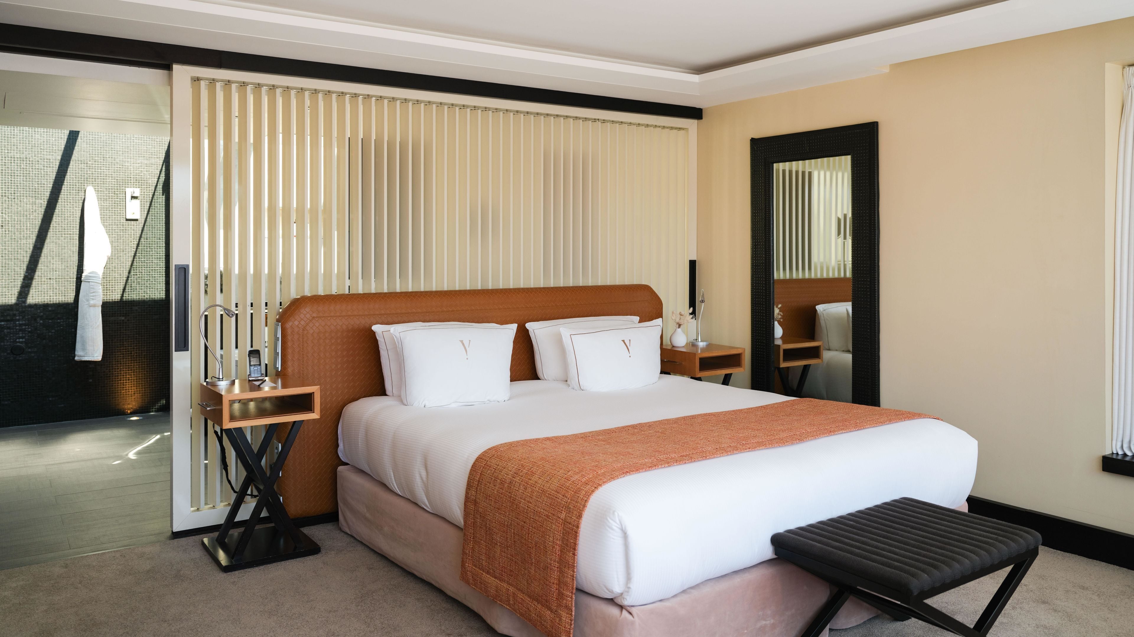 A hotel room with a large bed, a bedside table, a nightstand, a mirror, and a view of the outside.