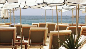 A beachside lounge area with rows of sun loungers and umbrellas, a sandy beach, and a view of the sea. - Five Seas by Inwood Hotels (Cannes)