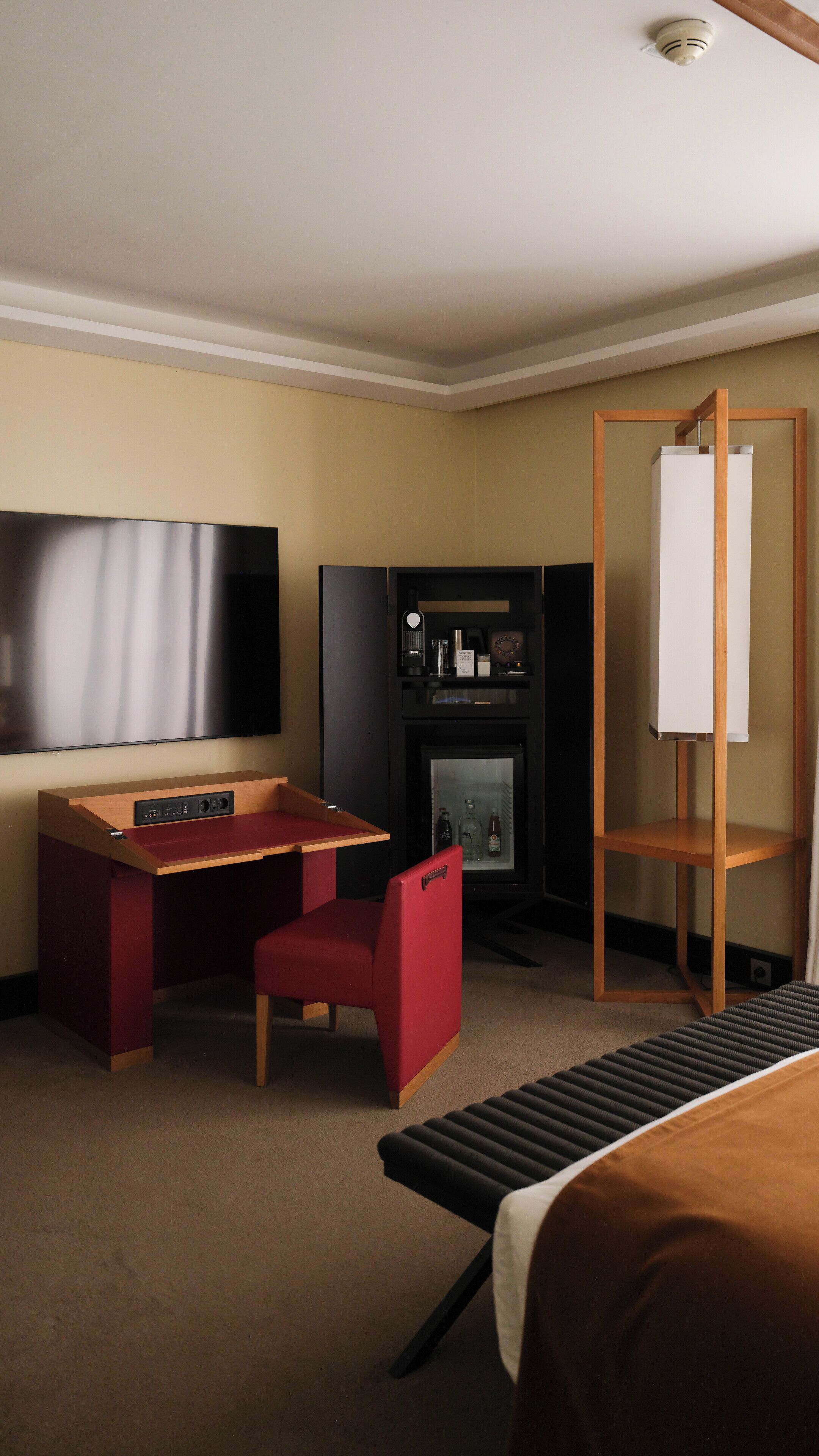 A hotel room with a bed, a desk with a chair, a television, a fireplace, and a whiteboard.
