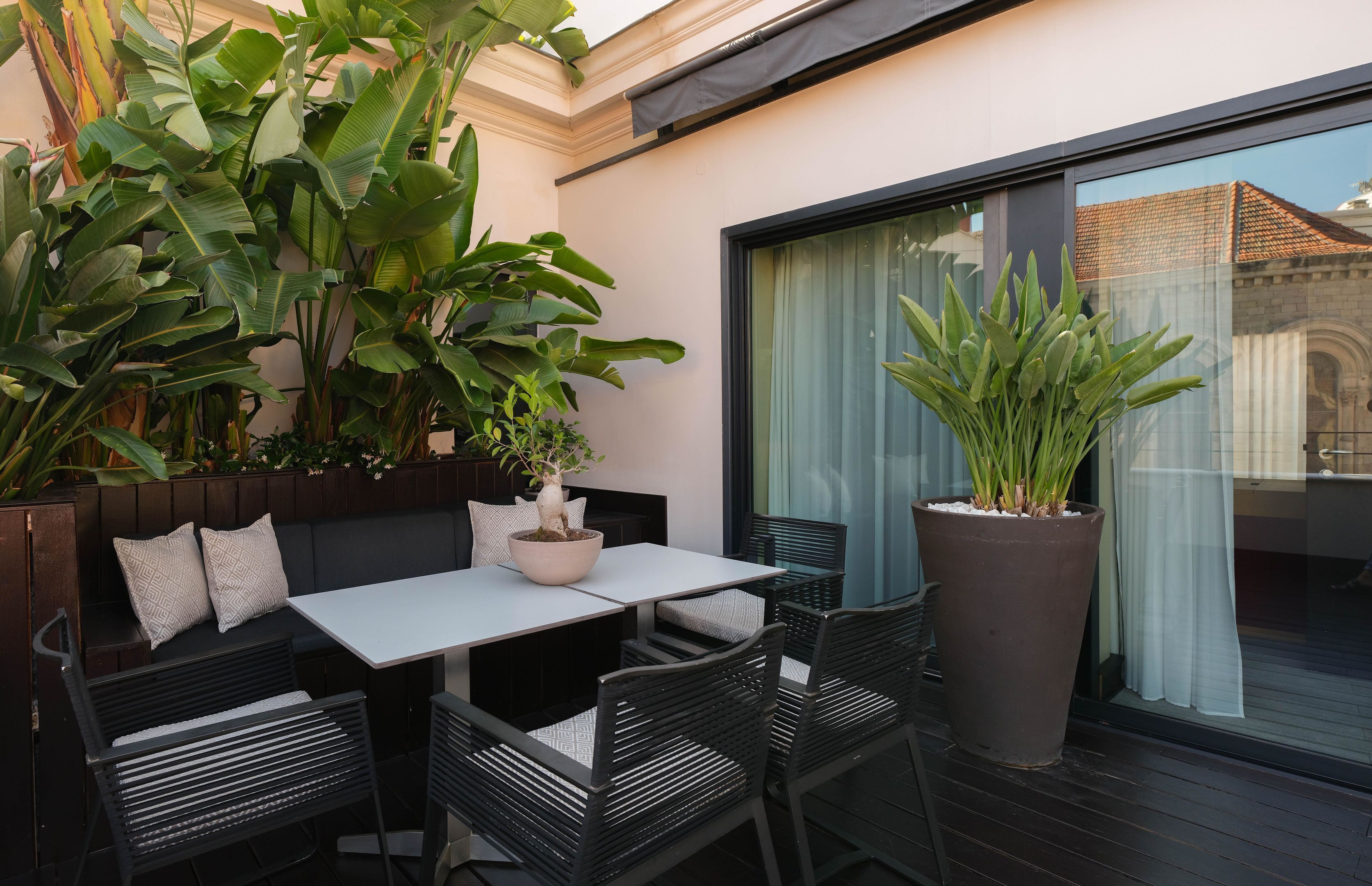 An outdoor seating area with a table and chairs, surrounded by large potted plants.