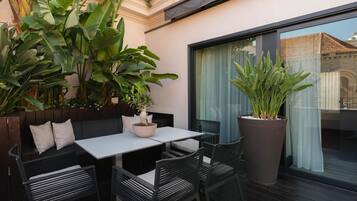 An outdoor seating area with a table and chairs, surrounded by large potted plants.