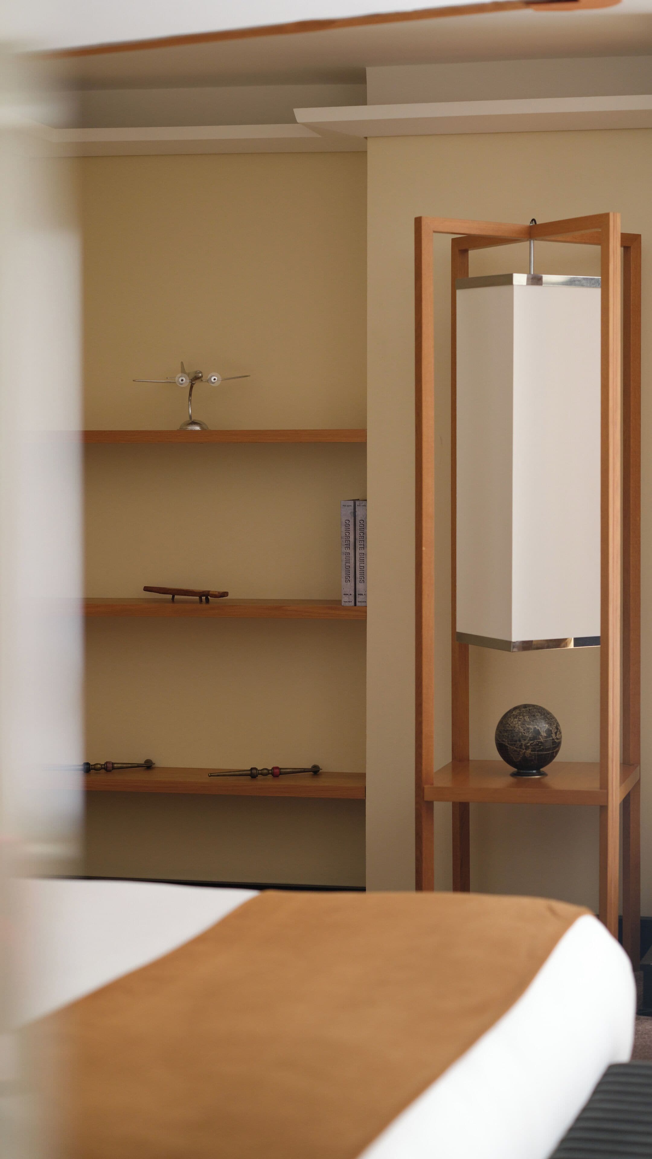 Una habitación de hotel con una cama, un estante de madera con un globo terráqueo y un libro titulado 'CONCRETE BUILDINGS'.