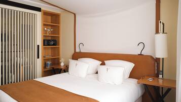 A hotel room with a bed, a bedside table, a lamp, a shelf with a radio, and a wardrobe.