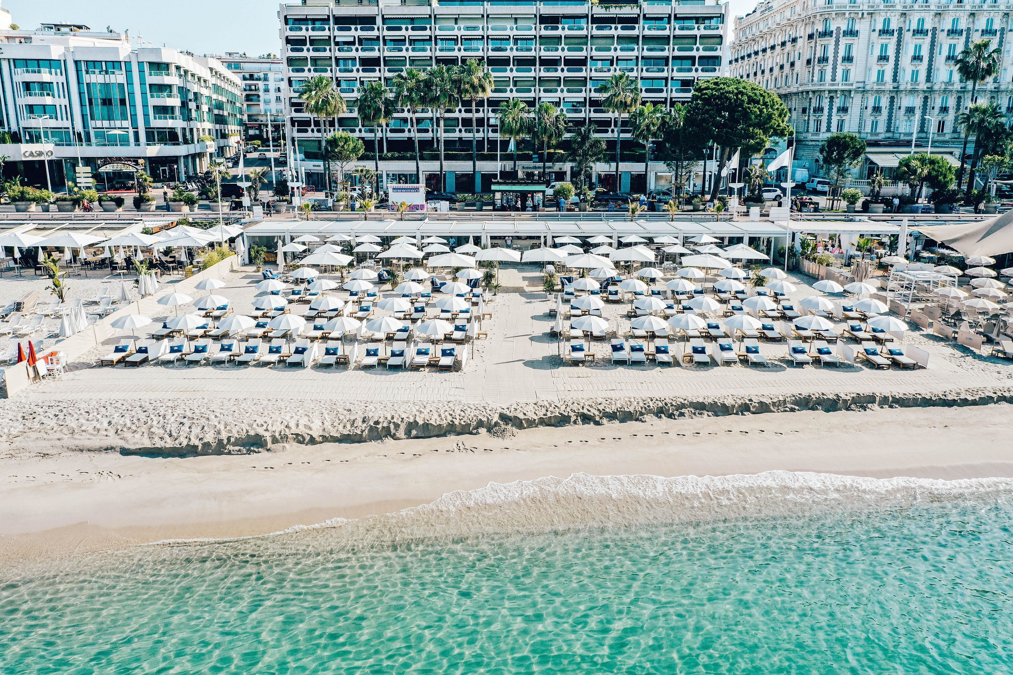 A beachside hotel with multiple sun loungers and umbrellas, a sandy beach, and a clear view of the ocean.