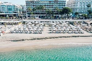 Un hotel frente a la playa con numerosas tumbonas y sombrillas, una playa de arena y una vista despejada del océano.
