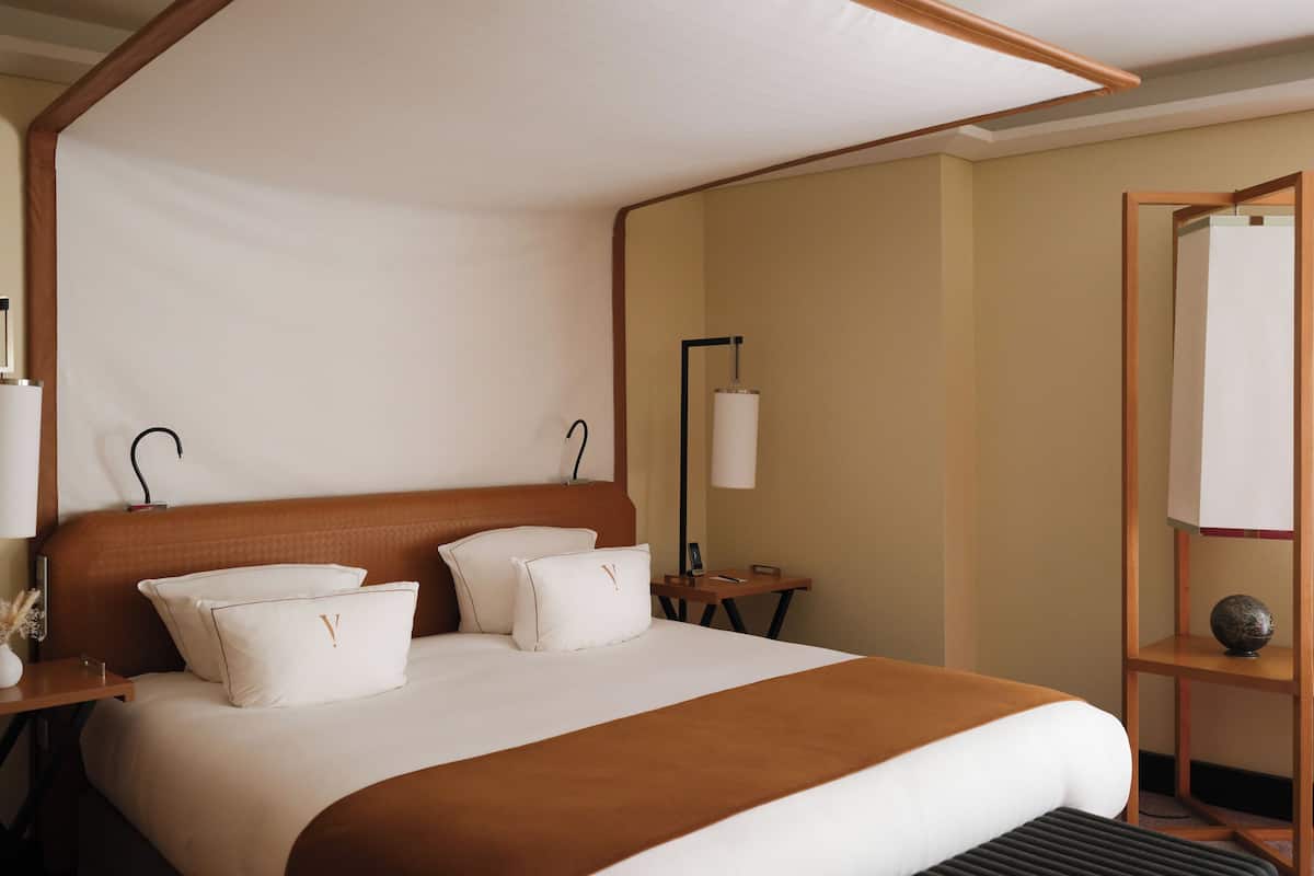 Habitación de hotel con una cama grande, dos mesitas de noche, un tocador, un espejo y una lámpara de noche.