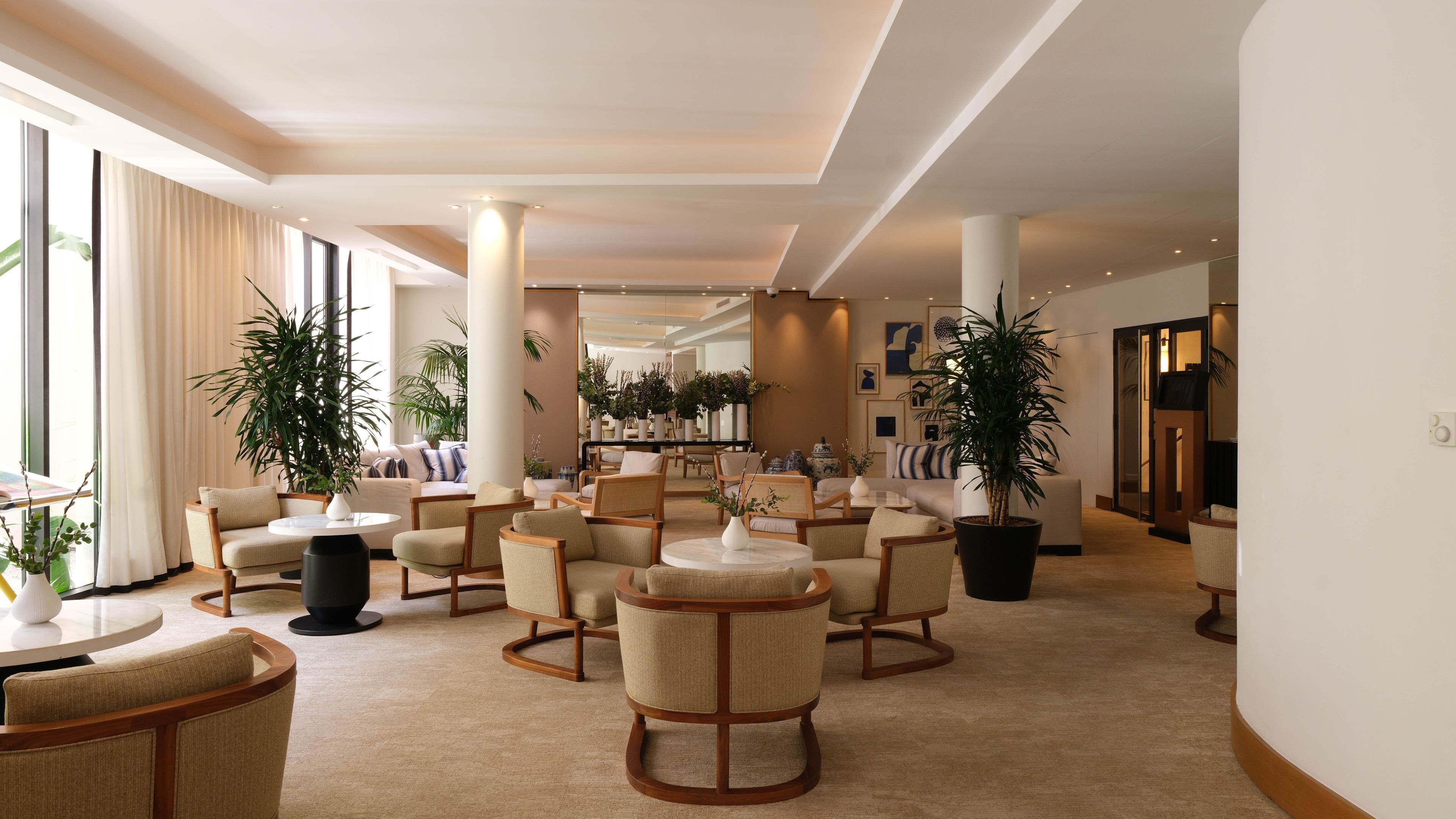 A hotel lobby with multiple seating areas, large windows, and potted plants.