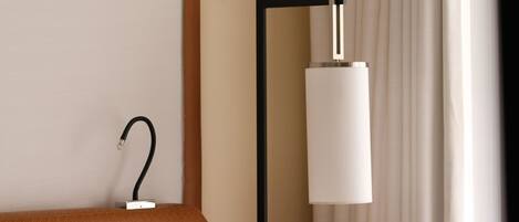 A hotel room with a bed, a nightstand, a lamp, and a window with curtains.