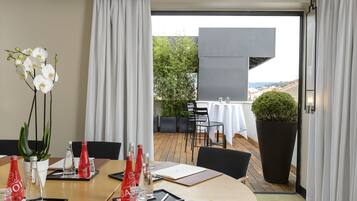 A modern hotel room with a dining area, a large potted plant, and a view of the cityscape.