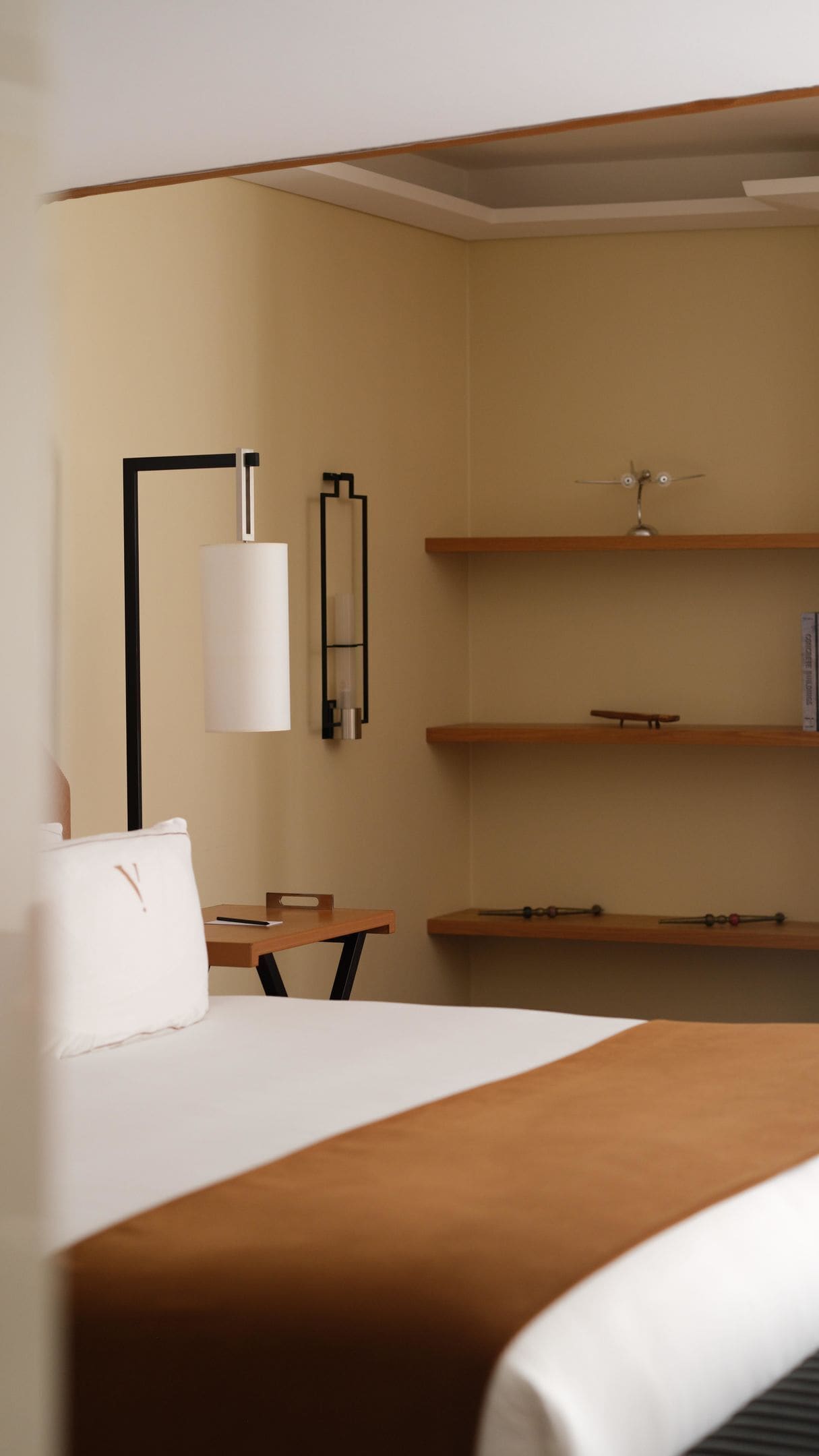 Ein Hotelzimmer mit Bett, Schreibtisch, Stuhl, Lampe und Regalen.