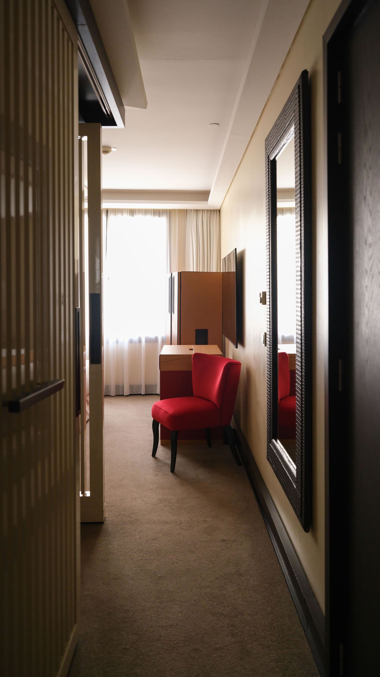 A hotel room with a bed, a desk, a chair, a large mirror, and a window with curtains.