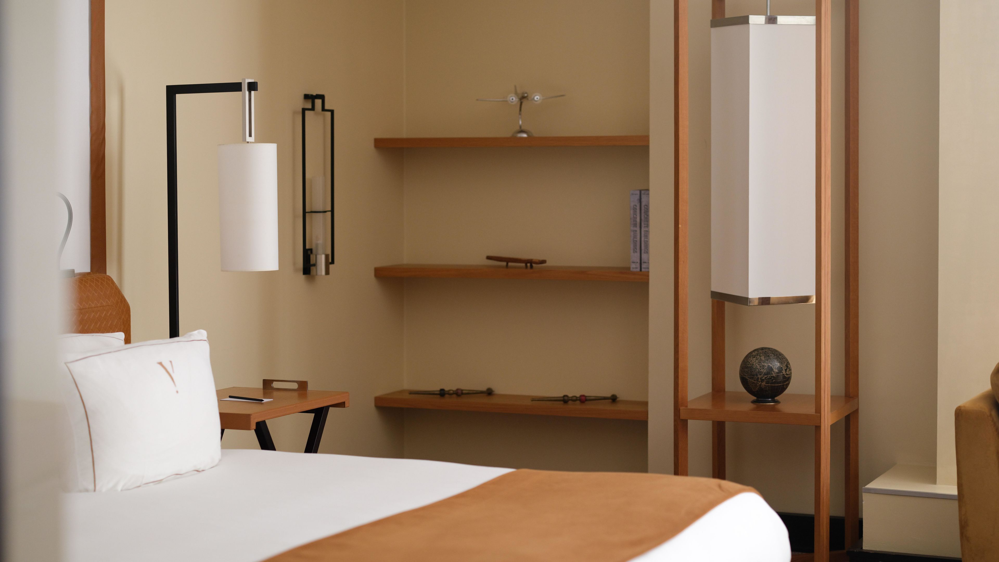 Una habitación de hotel con cama, escritorio, estantería con libros y un globo decorativo.