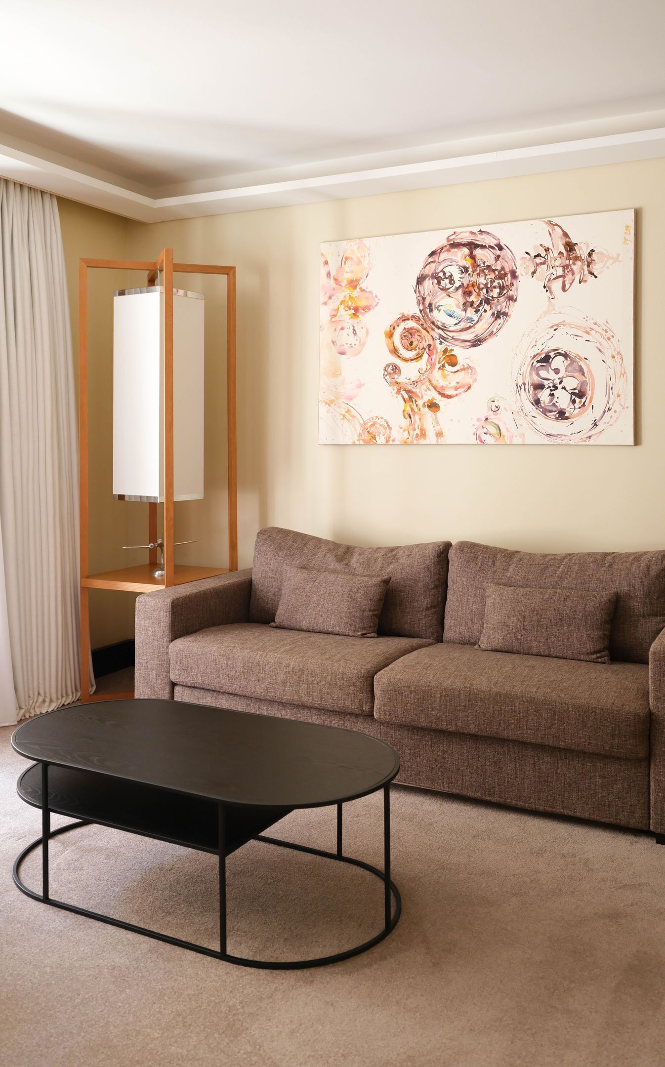 A living room with a brown sofa, a black coffee table, and a large abstract painting on the wall.