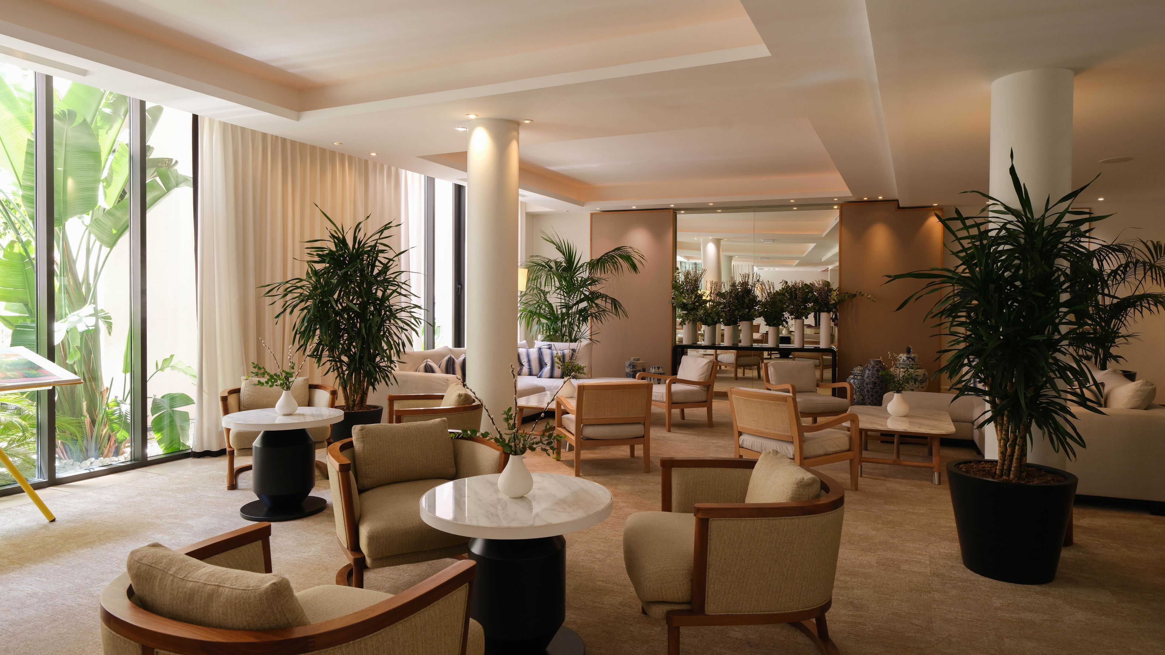 A hotel lobby with a seating area, large windows, and potted plants.