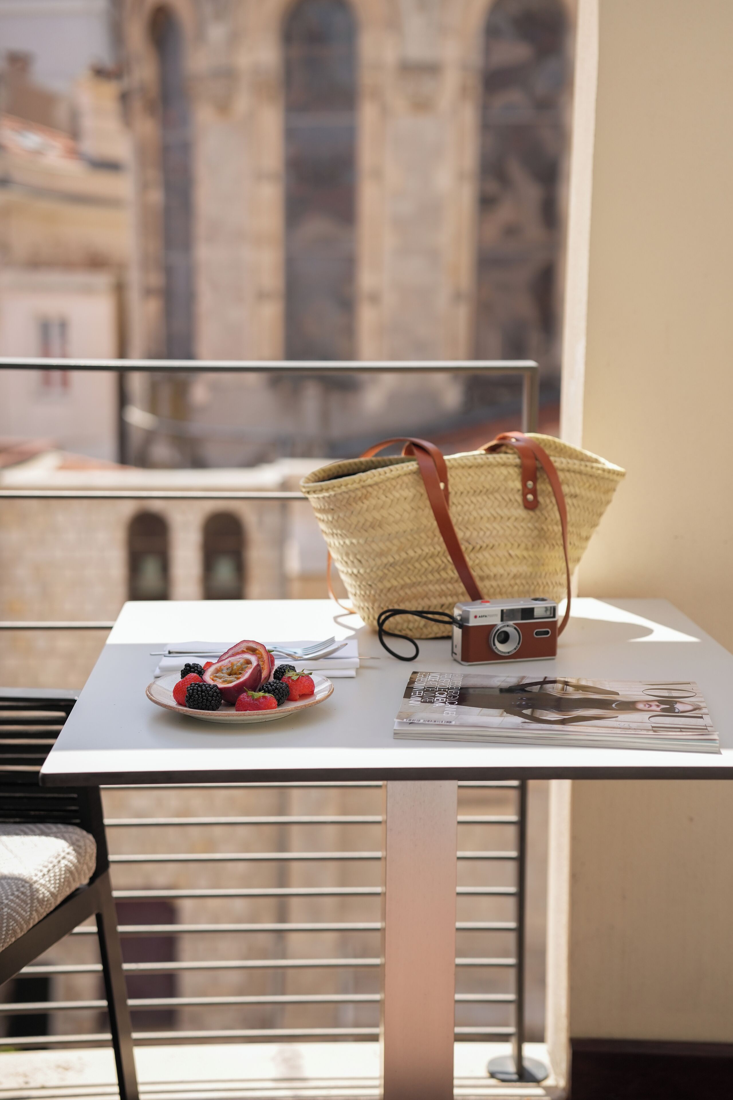 Un balcón con una mesa, una cámara, una cesta y un plato de fruta.