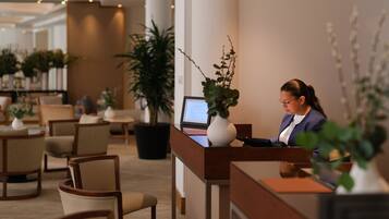 Taulell de recepció amb un ordinador, cadires i plantes en testos en un vestíbul d'hotel.
